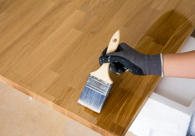 a man applying a coating of lacquer over wooden countertop