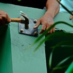 Worker using hammer on sleeve anchor bolt (expansion bolt) to cling steel plate into concrete beam.