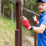 How Much Does It Cost to Install a Fence in 2026? worker installing welded metal mesh fence