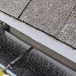 Do Brush Gutter Guards Work? Plastic guard brush in new dark grey plastic rain gutter on asphalt shingles roof.