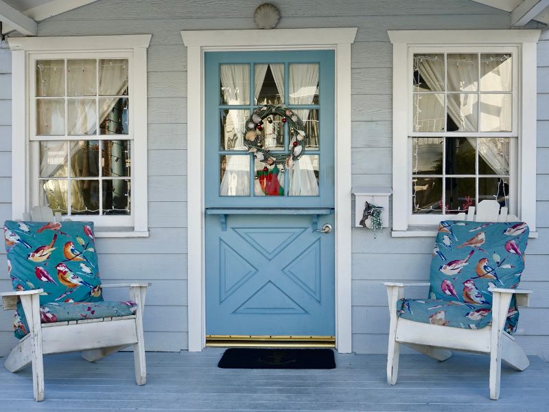 Light blue shiplap siding forms the exterior wall of a home, characterized by its distinct horizontal boards that create a subtle shadow line. The shiplap frames a blue Dutch door and two windows.
