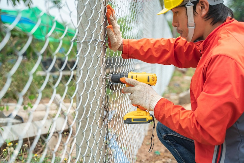 worker wear helmet and glove install wire mesh fence with screws drill