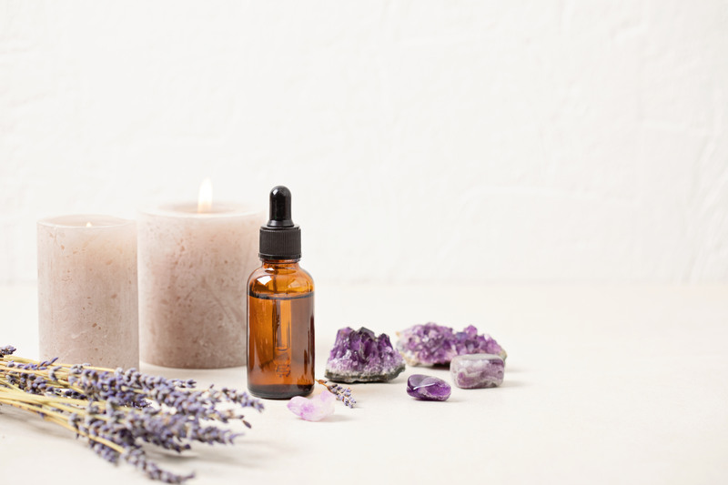 Glass bottle of lavender essential oil with lavender flowers and candles and amethyst crystals.