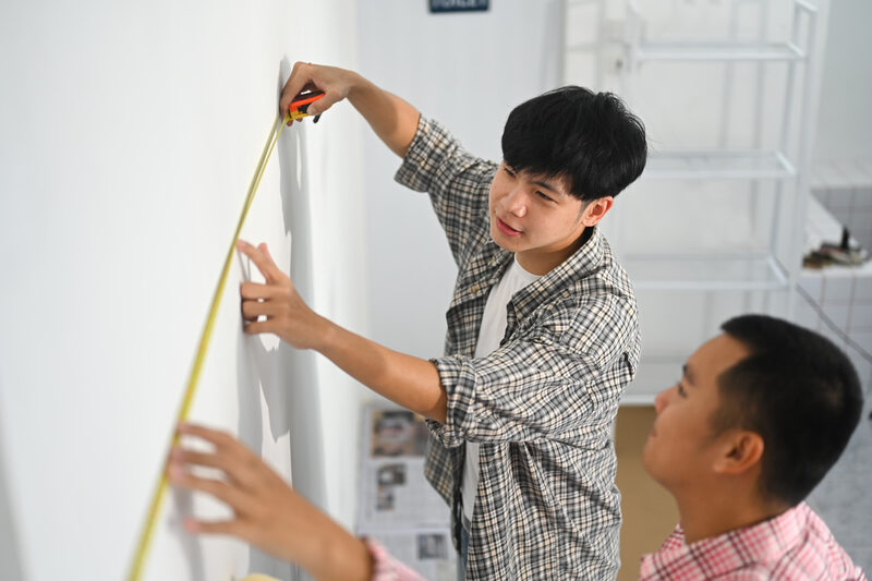 Two young men measuring a wall preparing for a home improvement project 
