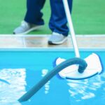 Male worker cleaning outdoor pool with underwater vacuum