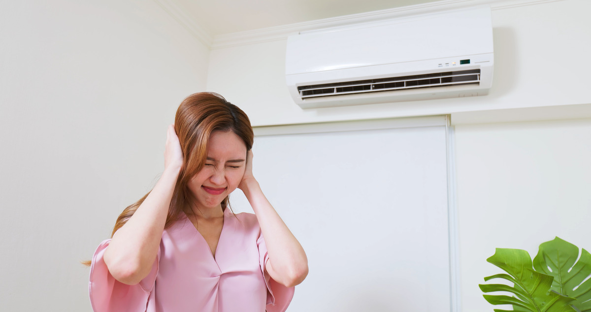 a woman closing her ears due to the noise caused by her air conditioner