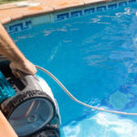 person pulling a robotic pool cleaner our of a swimming pool