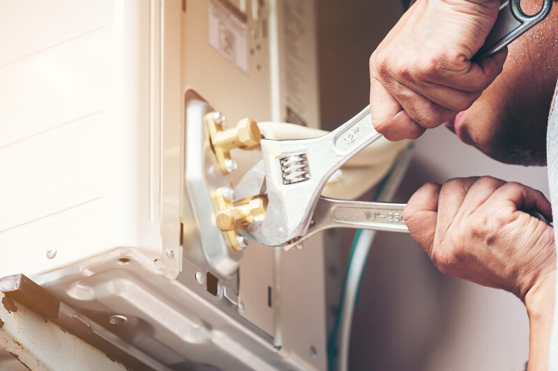 Technician hand using fix wrench to tighten loose bolts on outdoor AC unit.