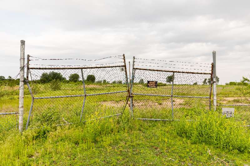 chainlink fence gate that is locked and bent out of shape, with no trespassing signs visible