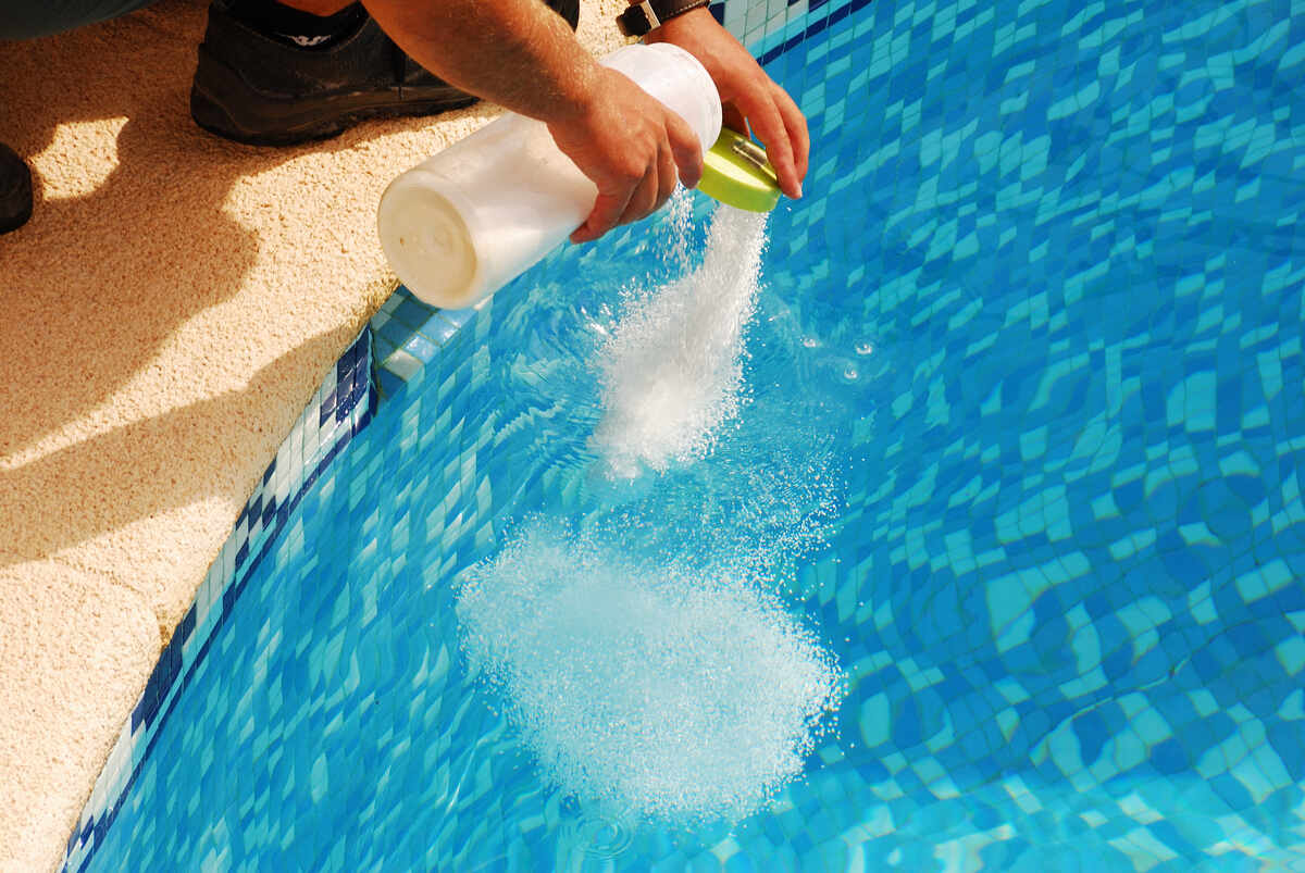 A person is pouring granular chlorine directly into a swimming pool for water disinfection.