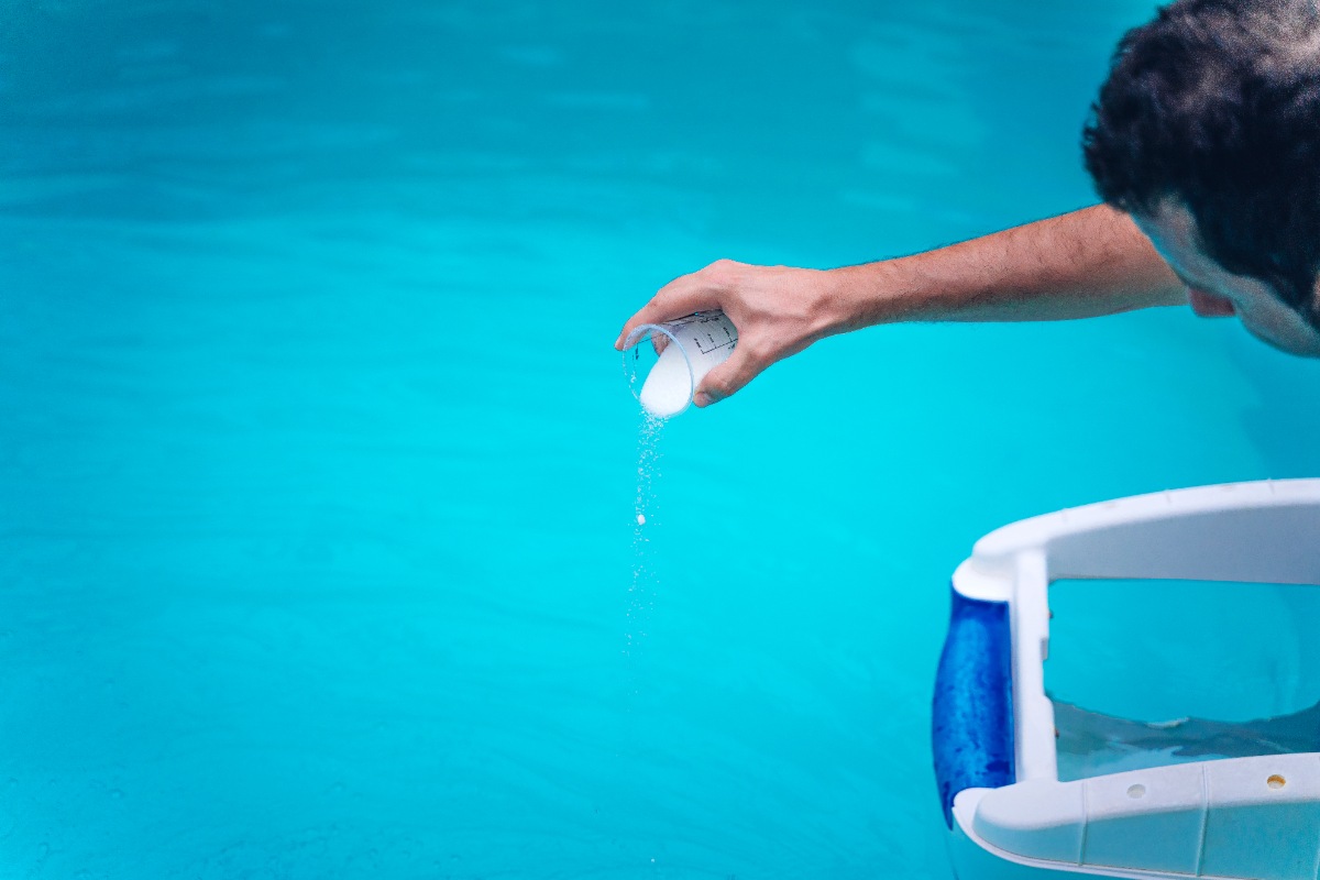 Person cleaning and chlorinating the pool on a hot summer afternoon
