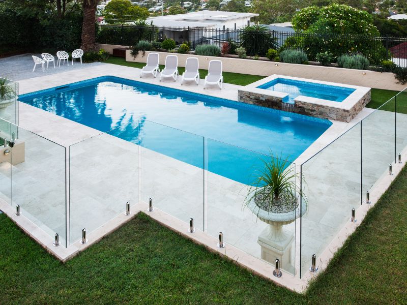 Modern swimming pool fenced in with glass panels beside a lawn 
