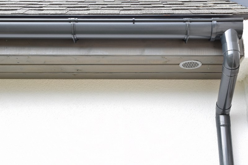 Gray half-round gutter with downspout attached to roof edge of modern house, designed for smooth water flow and drainage