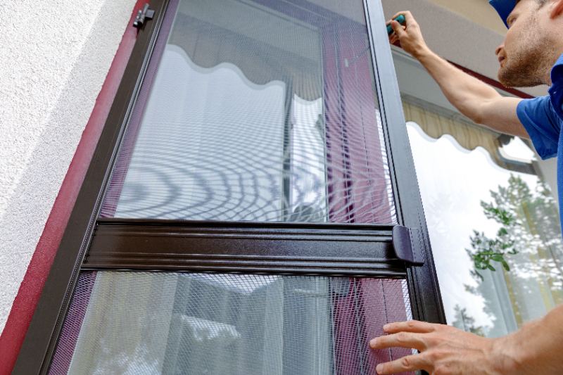 man installing mosquito net wire mesh on house balcony door