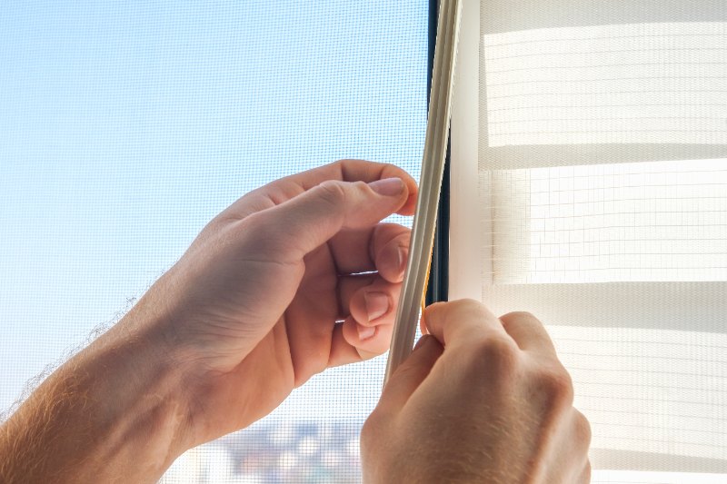 Close-up of hands applying adhesive-backed weather stripping to a window frame to improve sealing, insulation, and energy savings.