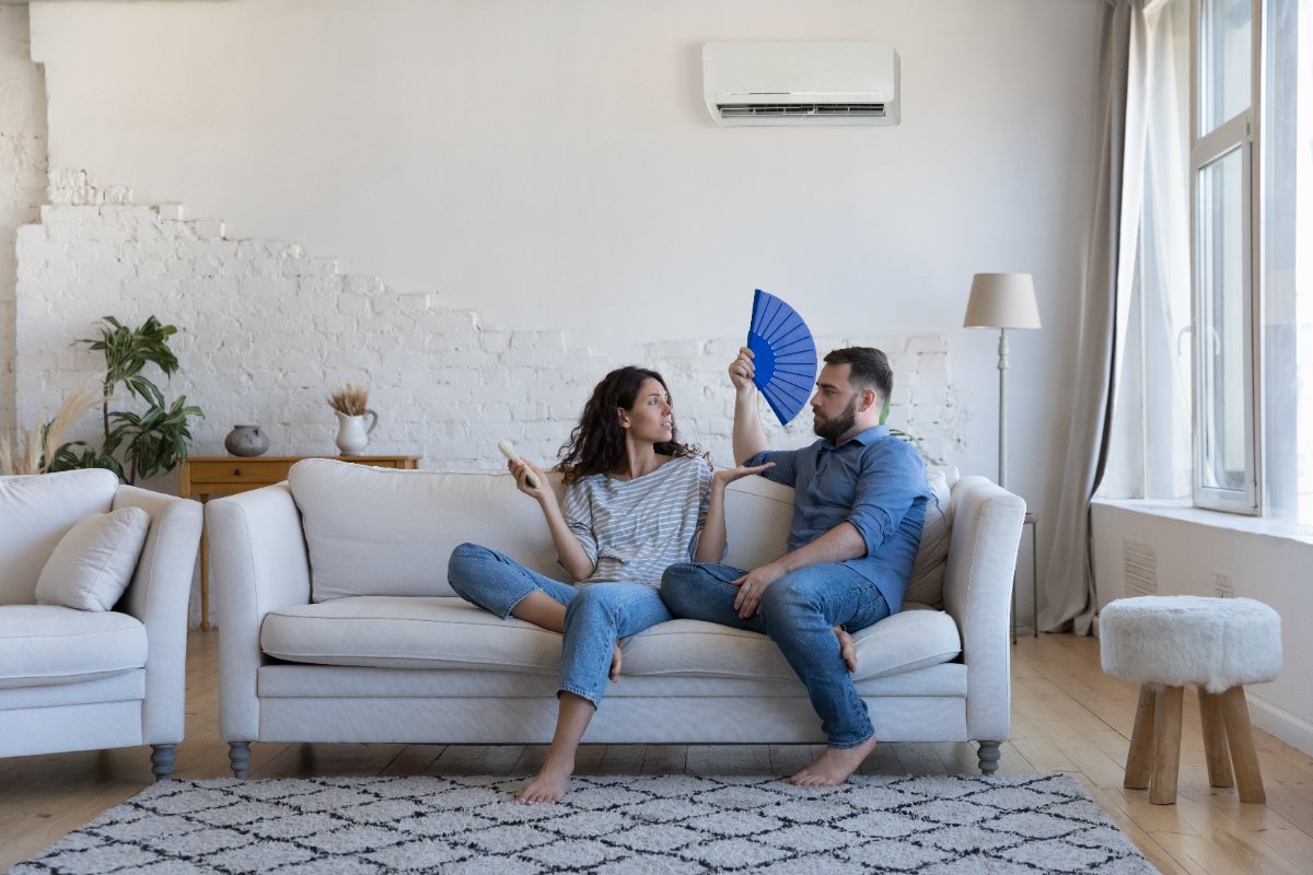 couple sitting on a couch fanning themselves to indicate a broken air conditioner unit
