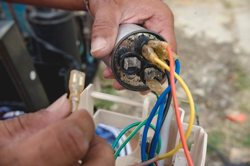AC technician removing a defective capacitor from a window type air conditioner control panel.