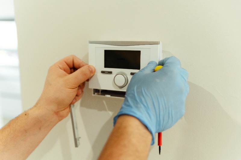 male electrician repairing thermostat in a smart home with a screwdriver.