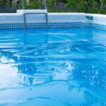 A large amount of water is pooling on top of a blue bubble solar cover on an above-ground swimming pool.