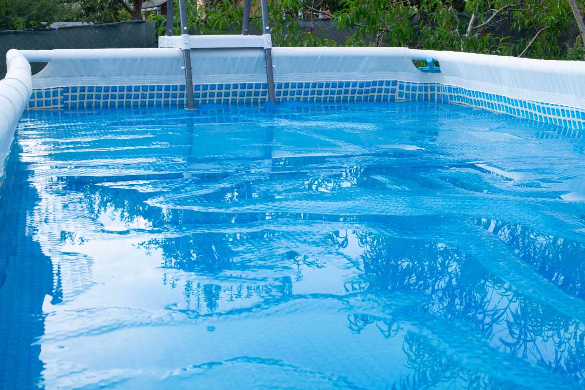 A large amount of water is pooling on top of a blue bubble solar cover on an above-ground swimming pool.