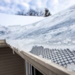 Ice and snow buildup forming an ice dam along a roof edge with a mesh gutter guard visible, highlighting winter gutter problems.