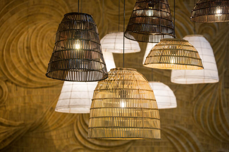 A cluster of hanging pendant light fixtures with shades woven from natural materials like bamboo and rattan, casting a warm light against a textured wall.