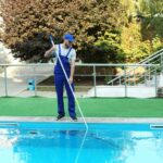 Male worker cleaning outdoor pool with scoop net